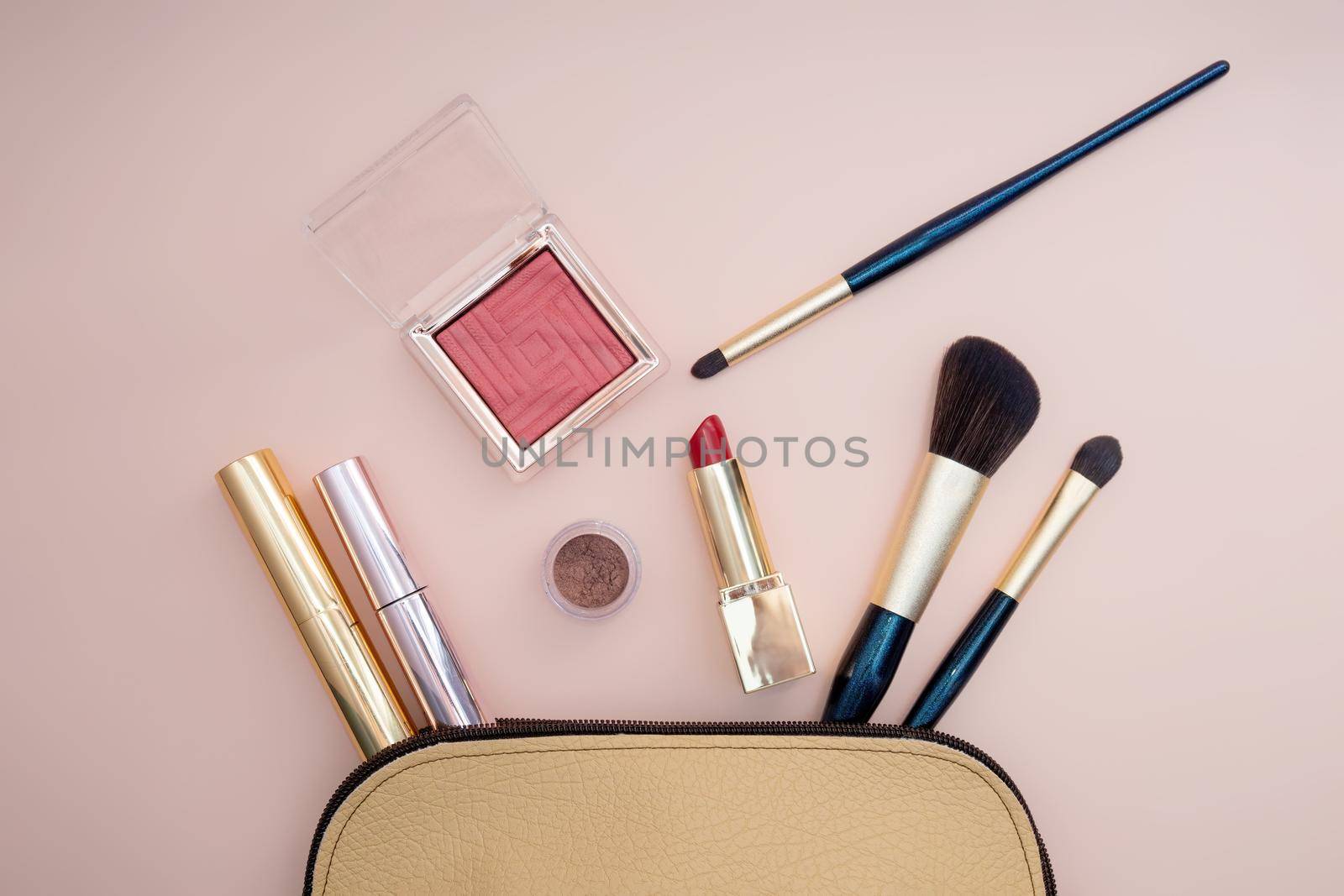 Top view of cosmetics standing out from beige makeup bag on pink background. Photo