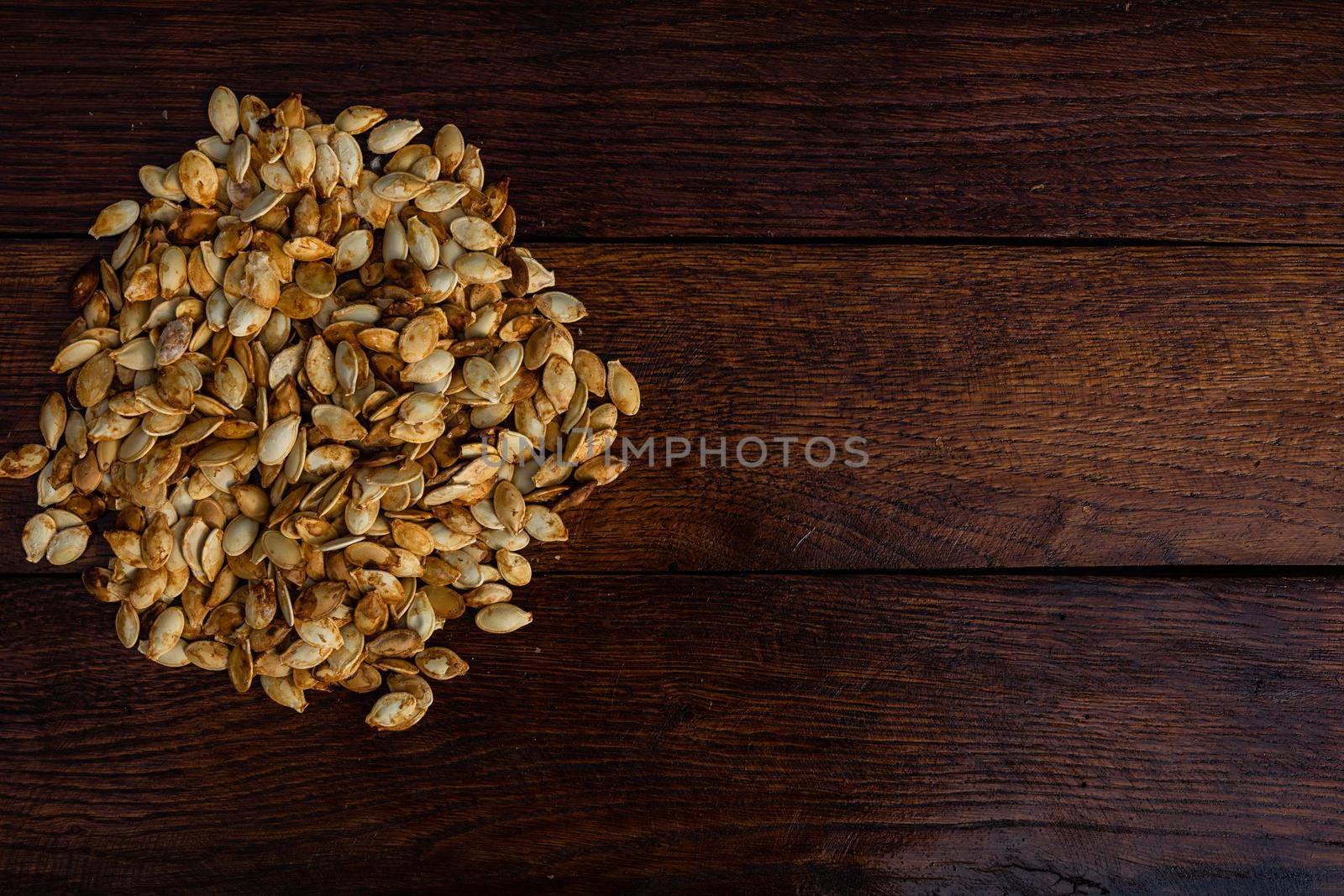 Roasted and salted pumpkin seeds on a wooden board. by vladispas