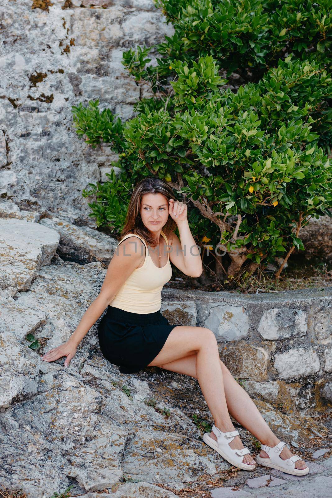 Beautiful girl sits on the stone wall of the old town of Budva . The girl sits on a stone parapet, Budva, Montenegro