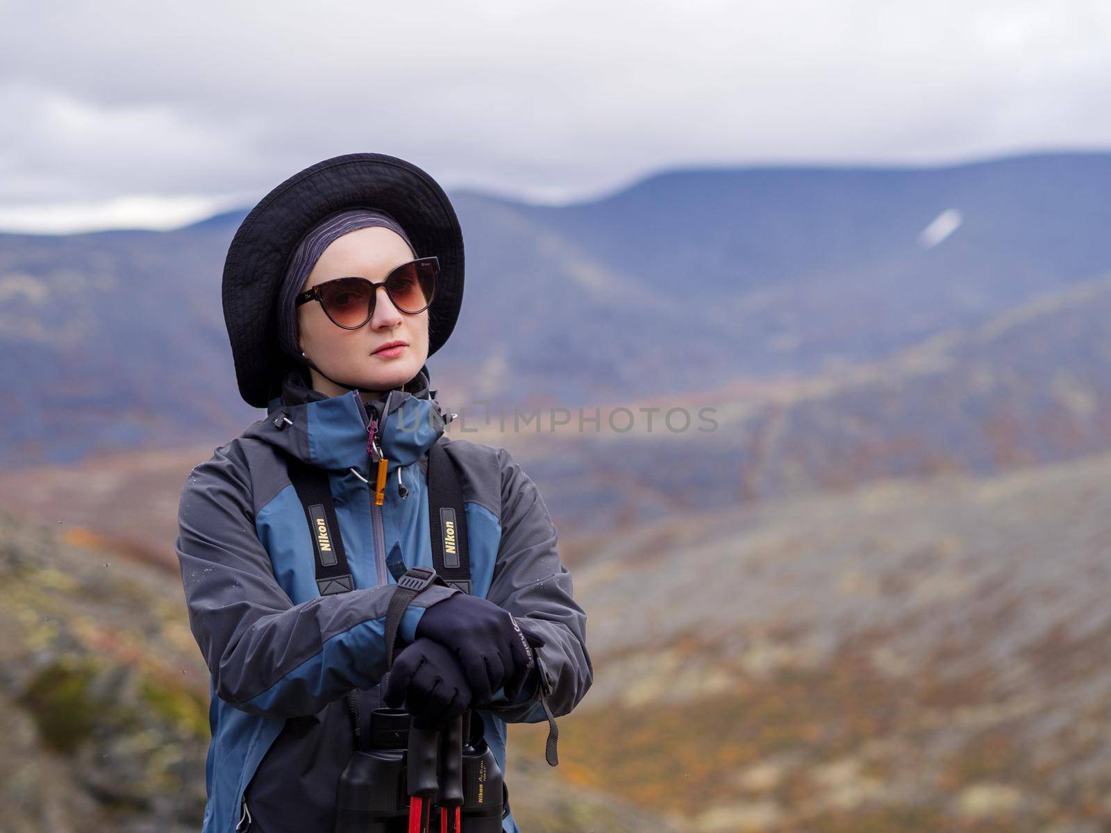 Young woman mountain tourist in glasses with trekking poles on the background of mountains.