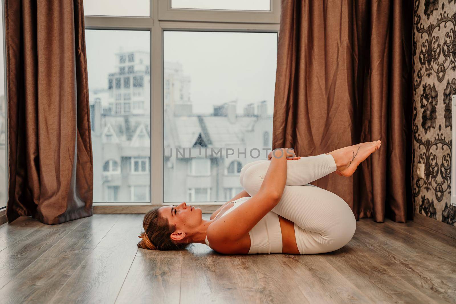 Young athletic attractive woman practicing yoga. Works out at home or in a yoga studio, sportswear, white pants and a full-length top indoors. Healthy lifestyle concept.