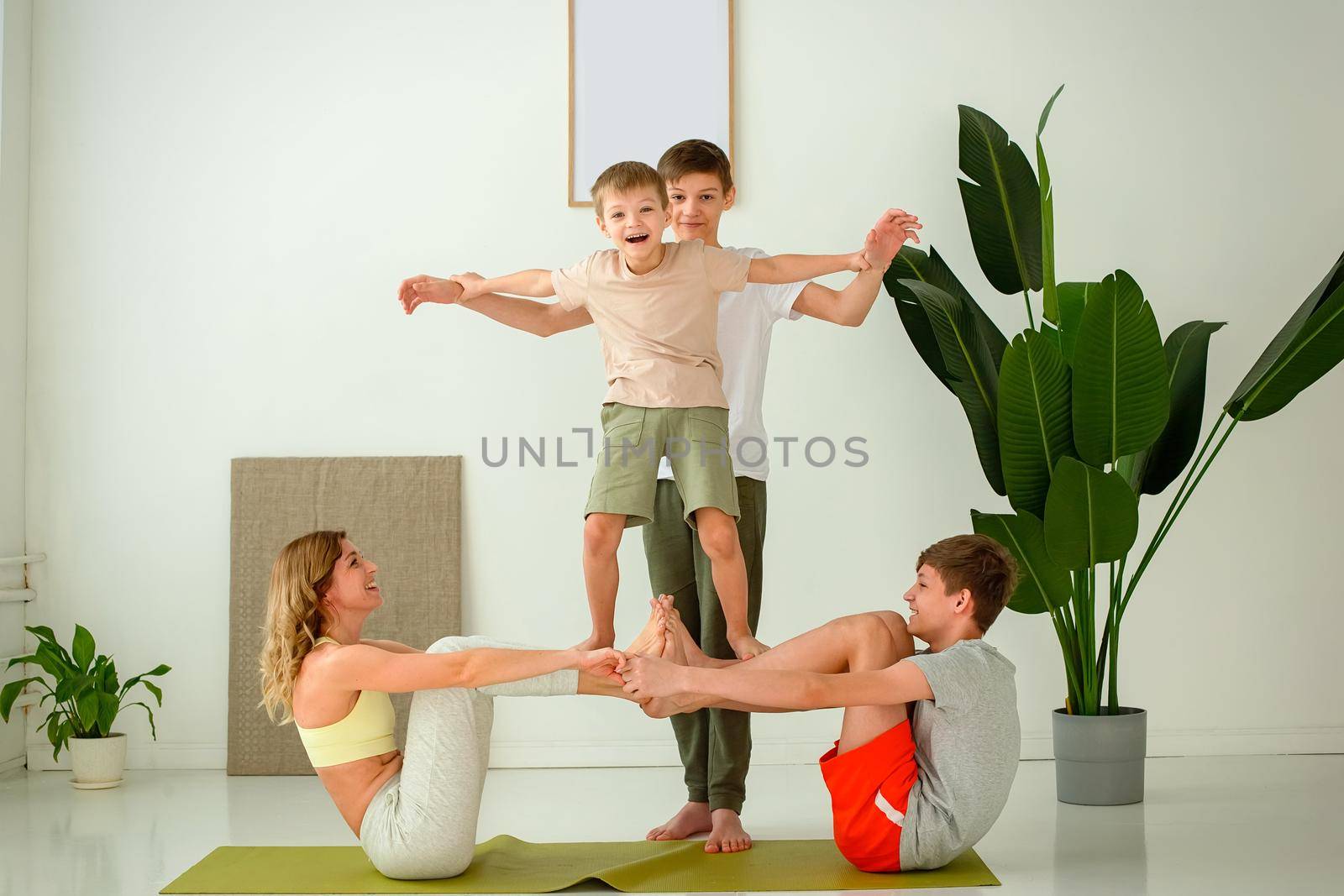 Sports happy family, a slim woman, a boy and two teenagers perform group yoga exercises with support while sitting on a sports mat. copy space