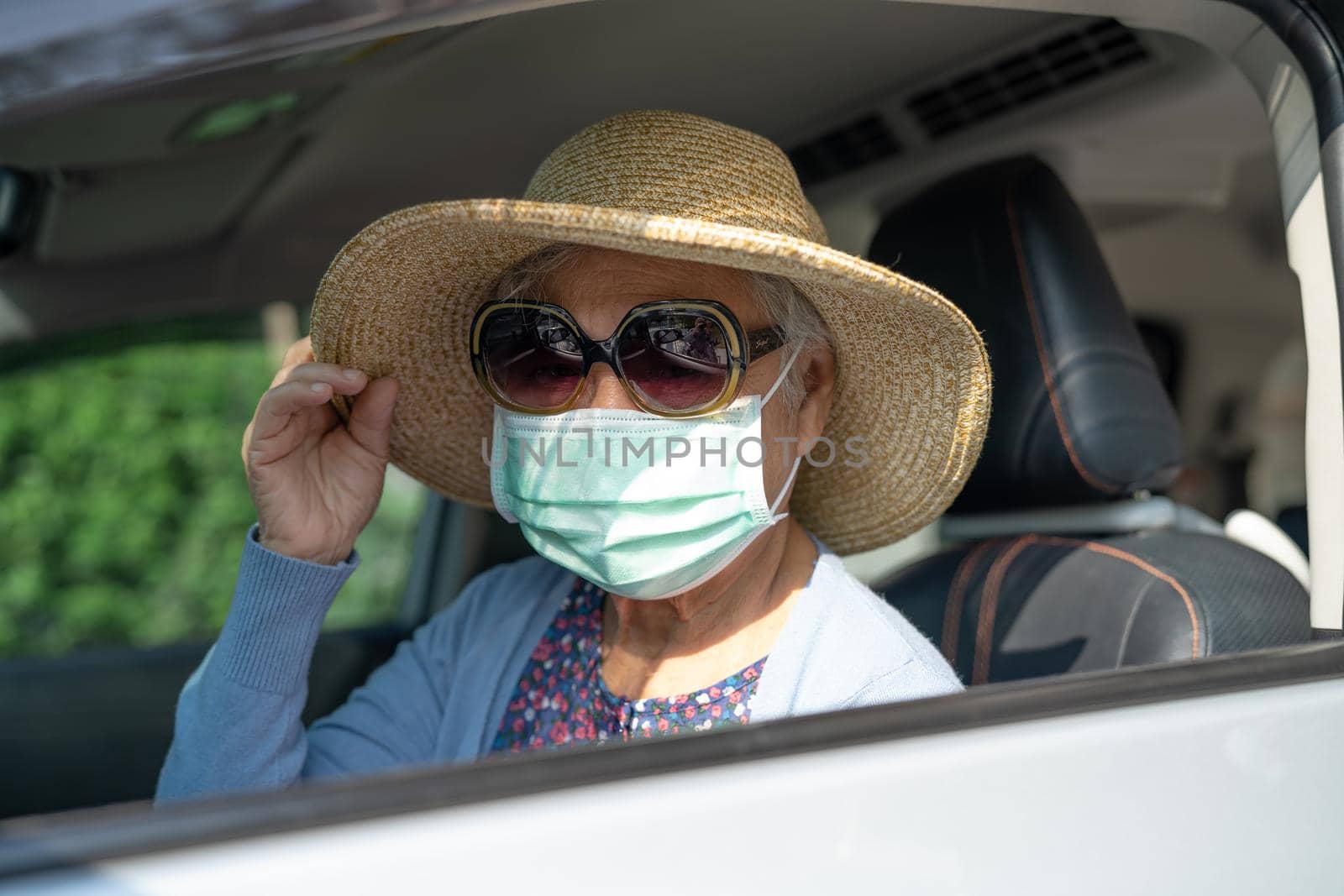 Asian elderly woman with mask and hat sitting in car with enjoy and freedom in traveling trip.
