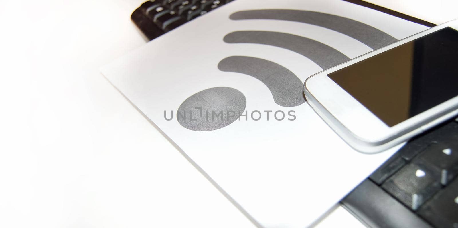 Wi-Fi symbol on a piece of paper near the computer keyboard and mobile phone, wireless Internet, copy space.