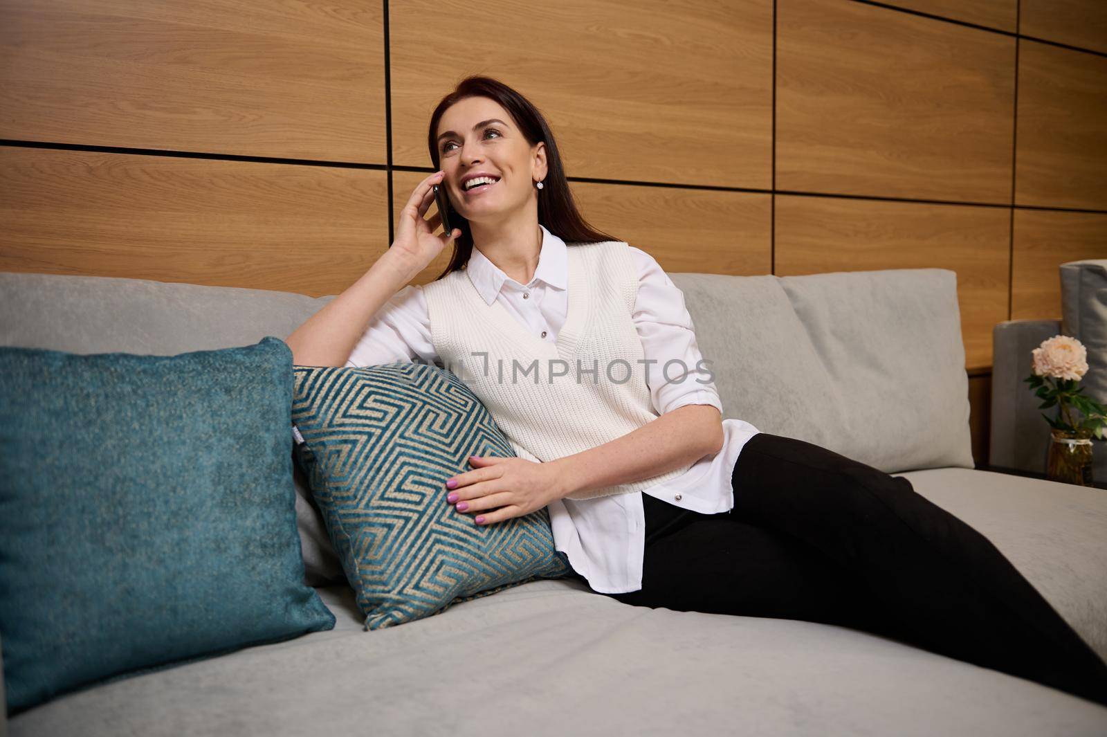 Elegant woman in casual clothes talks on a mobile phone, sits on a stylish sofa in a furniture mall, discusses a new home improvement project and agrees on a delivery time for materials for work by artgf