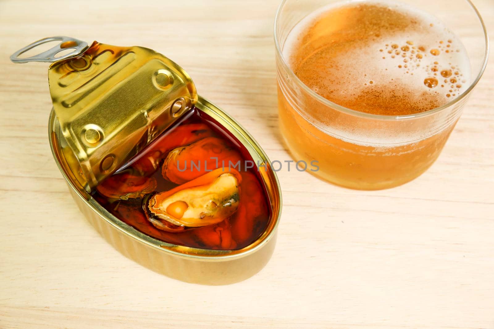 Can of tasty pickled mussels next to cold beer on wooden table