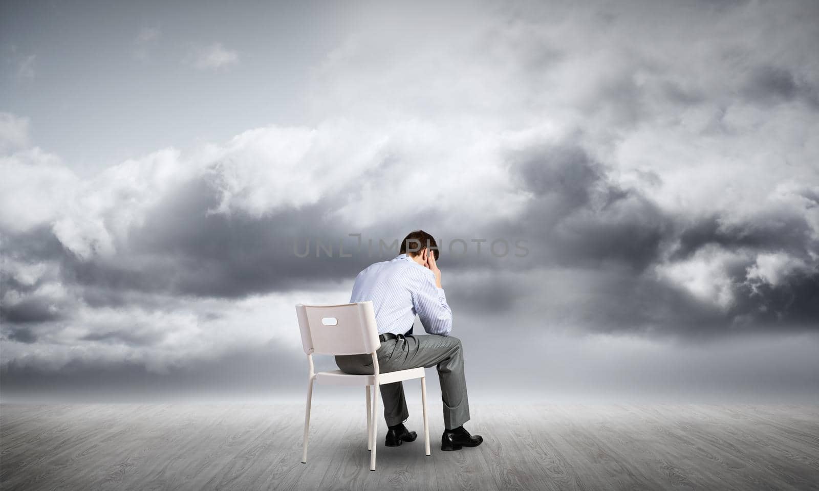 Businessman sitting on an office chair with his back, thinking and holding his head