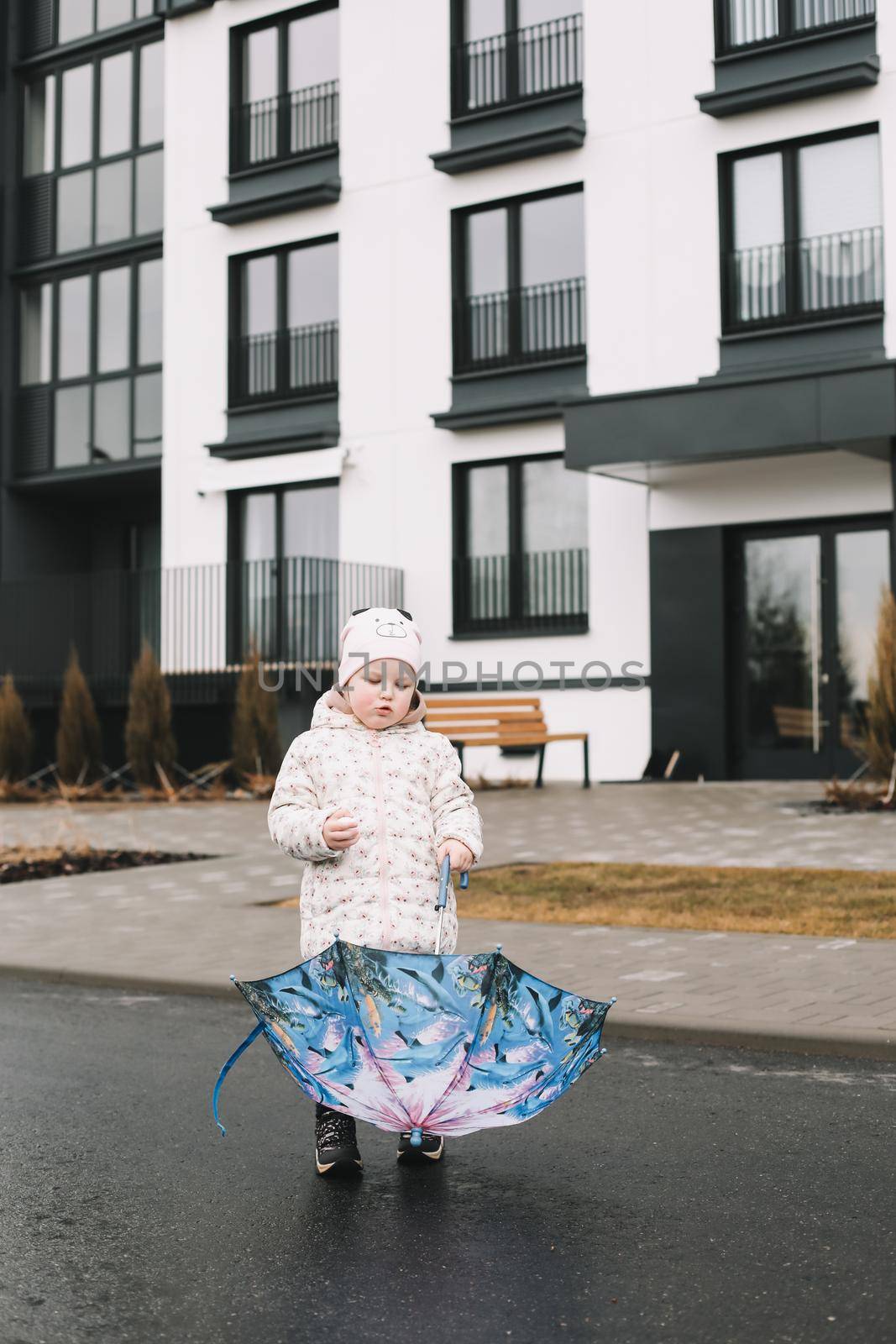 Toddler girl with colorful umbrella outdoors at rainy day.