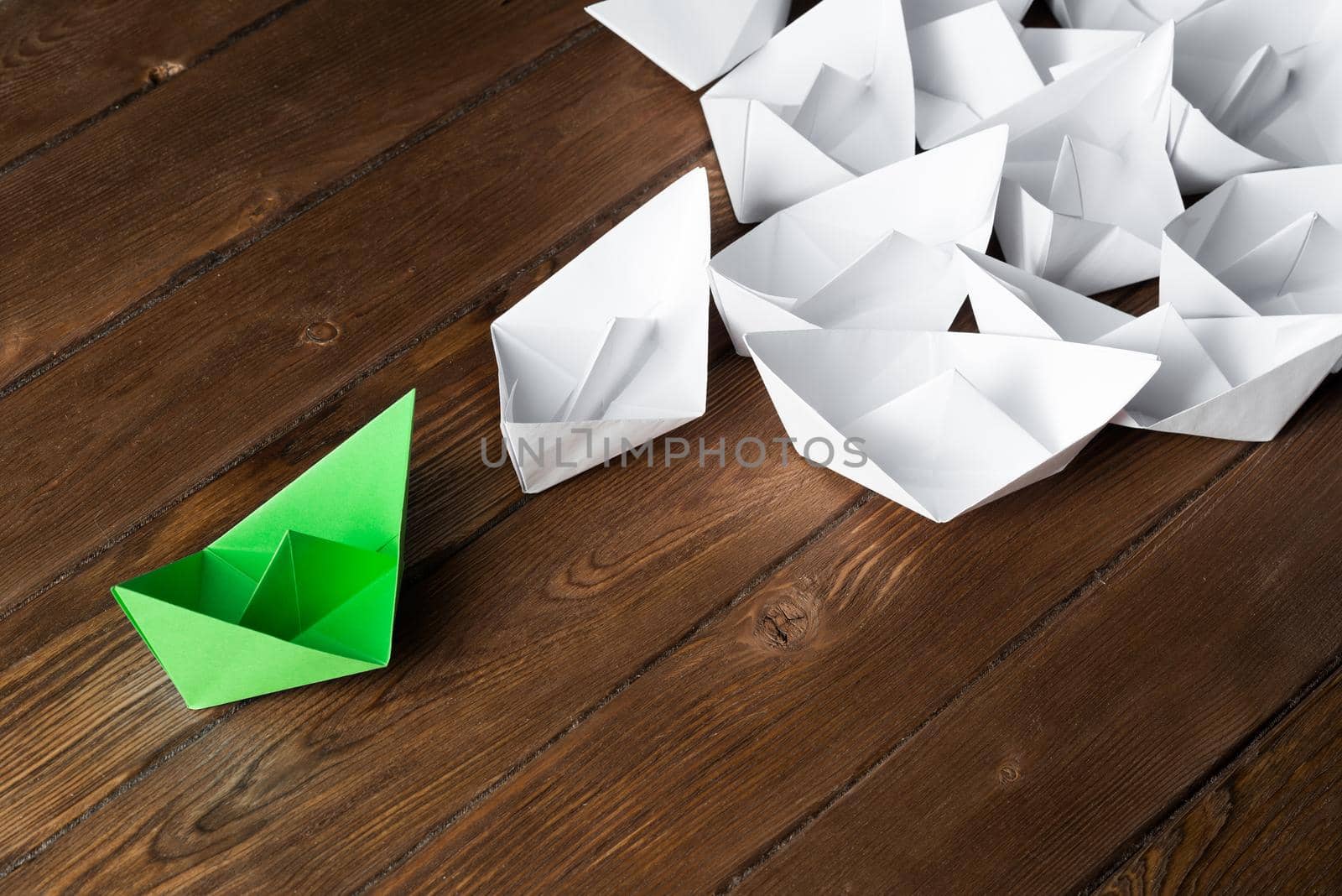 Business leadership concept with white and color paper boats on wooden table by adam121