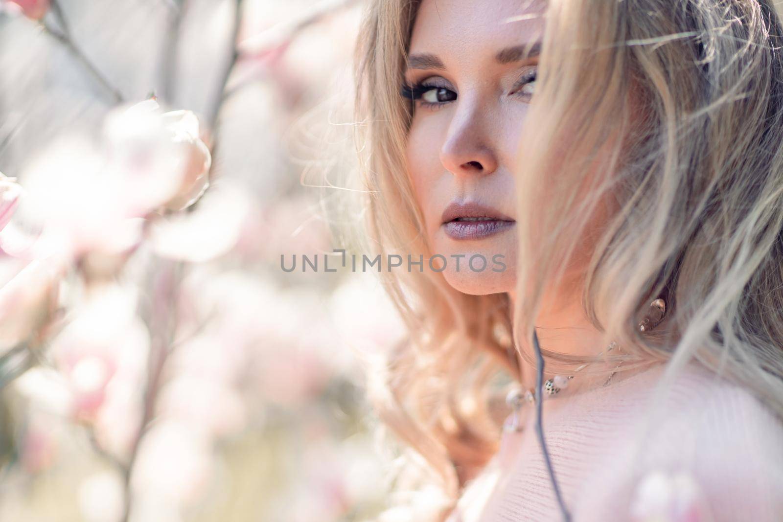 Portrait of a beautiful happy middle aged woman enjoying the smell in a blooming spring garden. Beautiful magnolia bushes, large flowers. by Matiunina