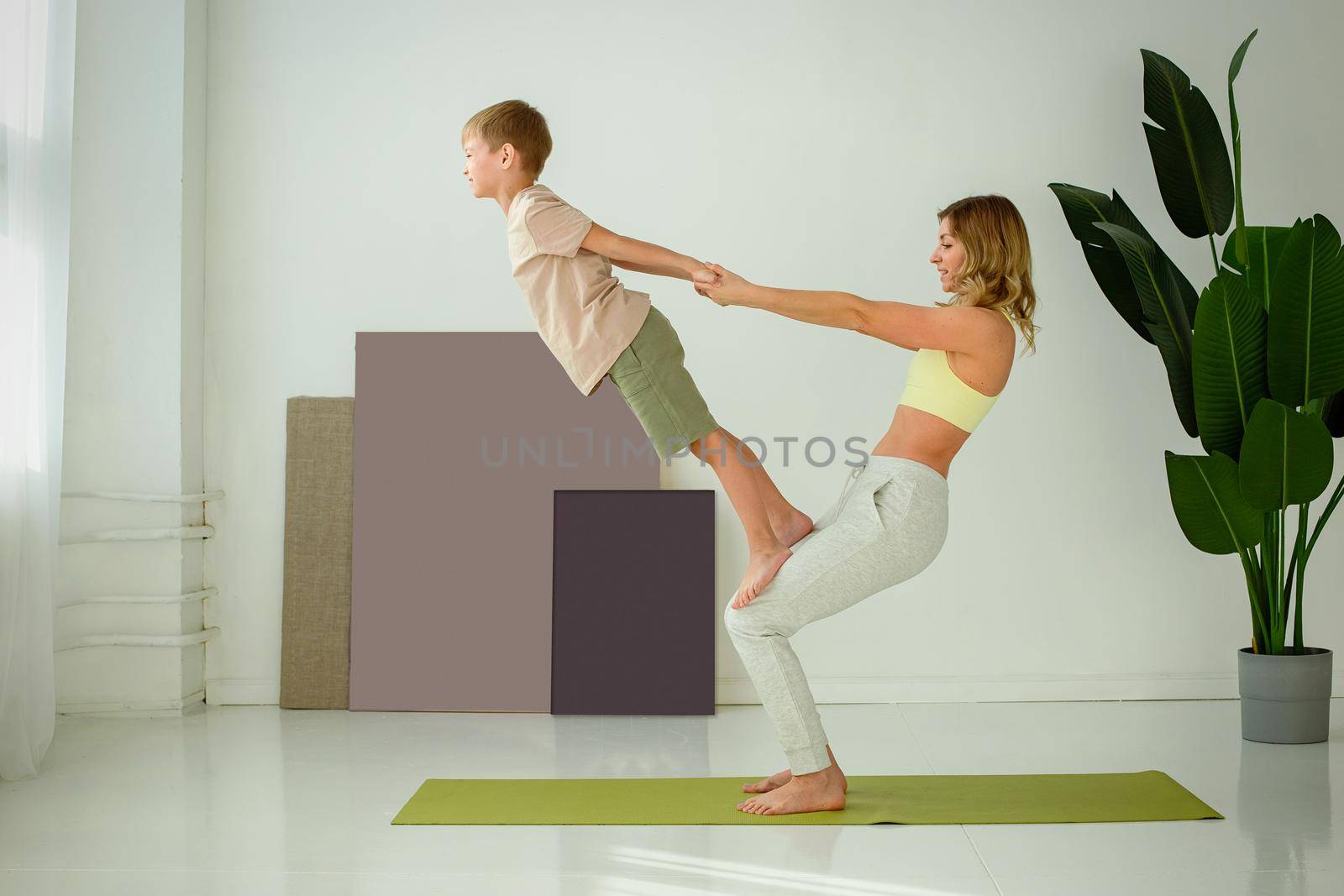 A beautiful slender woman, doing yoga with a child boy, doing exercises with support. copy space.