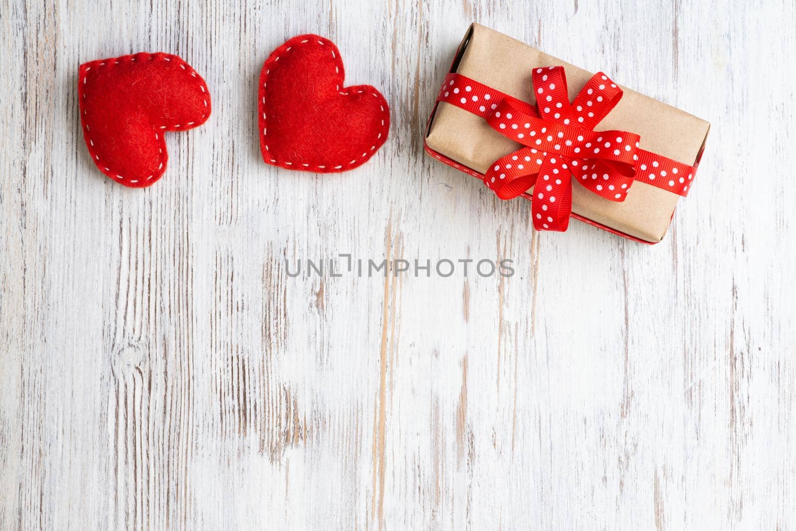 Flat lay cute composition with handmade fabric red hearts. Gift box with ribbon bow on wooden table. Happy birthday or anniversary congratulation. Romantic message template with copy space.