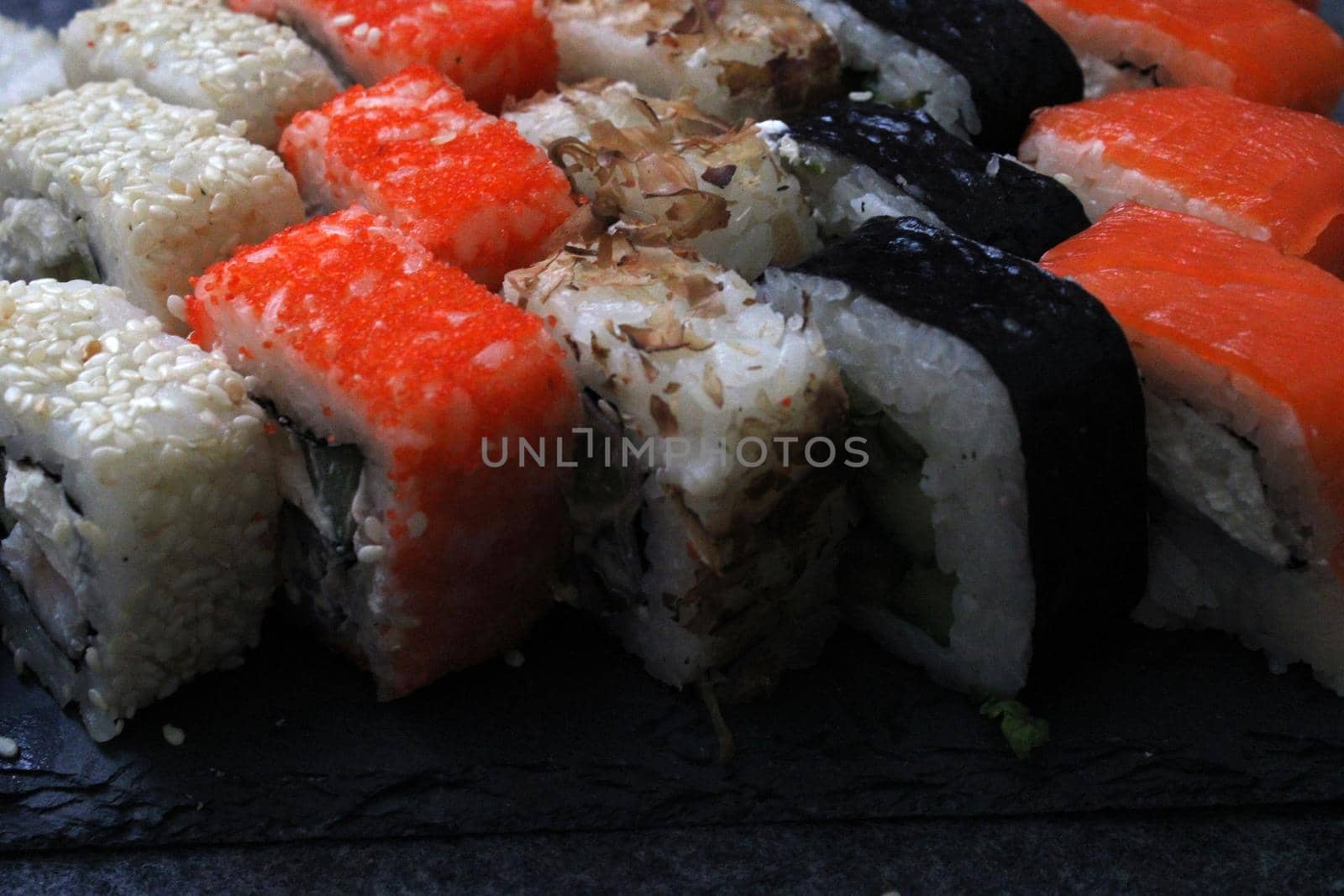 Rolls with shrimp, sesame, tuna, bacon, cheese, cucumber, vegetables and sushi sticks on a black board. Close-up. Japanese cuisine. Background.