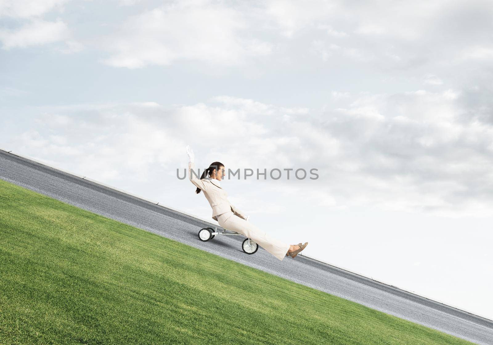 Beautiful happy woman riding downhill on road. Young employee in white business suit going down on small bike outdoor. Fast business startup. Beginner level business concept with bicyclist