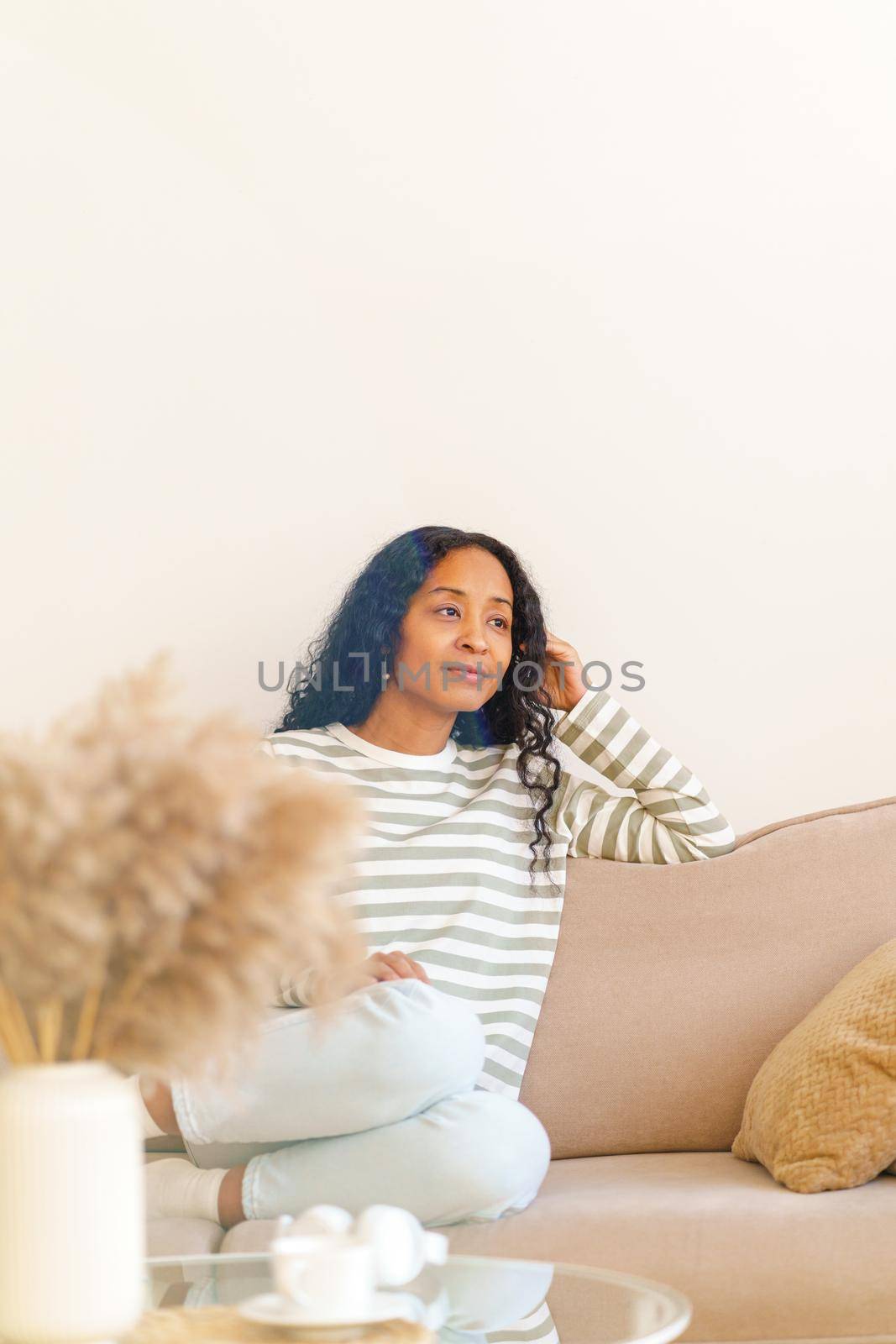 Dreaming and smiling African-American female sitting on sofa in lounge. Showing positive emotion. Concept of enjoying life in moment. Daytime pleasure and comfort. Selective focus copyspace vertical