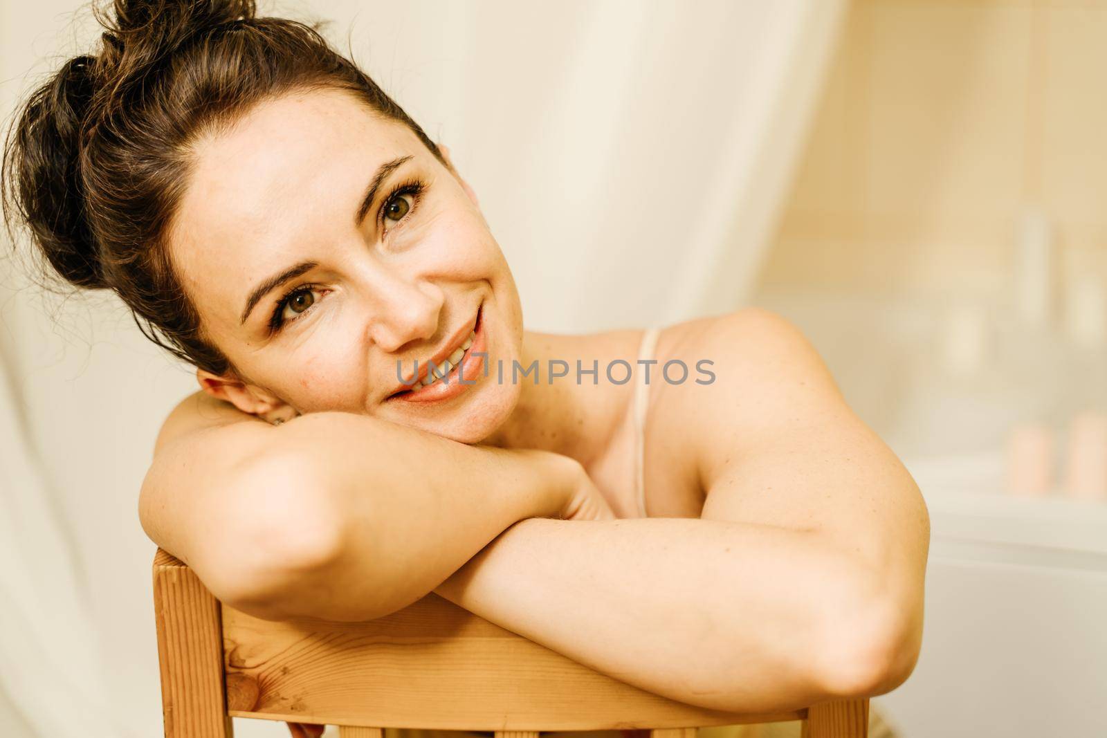 Portrait of a middle-aged woman, smiling with her arms folded in front of her face, her hair pulled up. The brunette is in a good mood. On a light background