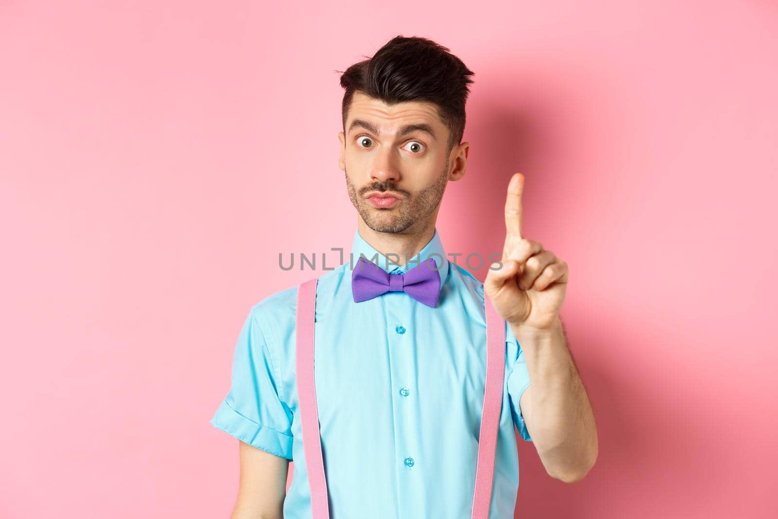 Young funny guy showing finger to explain something, prohibit or warn you, standing on pink background by Benzoix