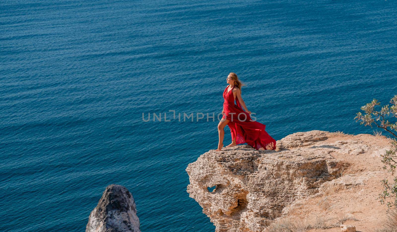 A woman in a red flying dress fluttering in the wind, against the backdrop of the sea