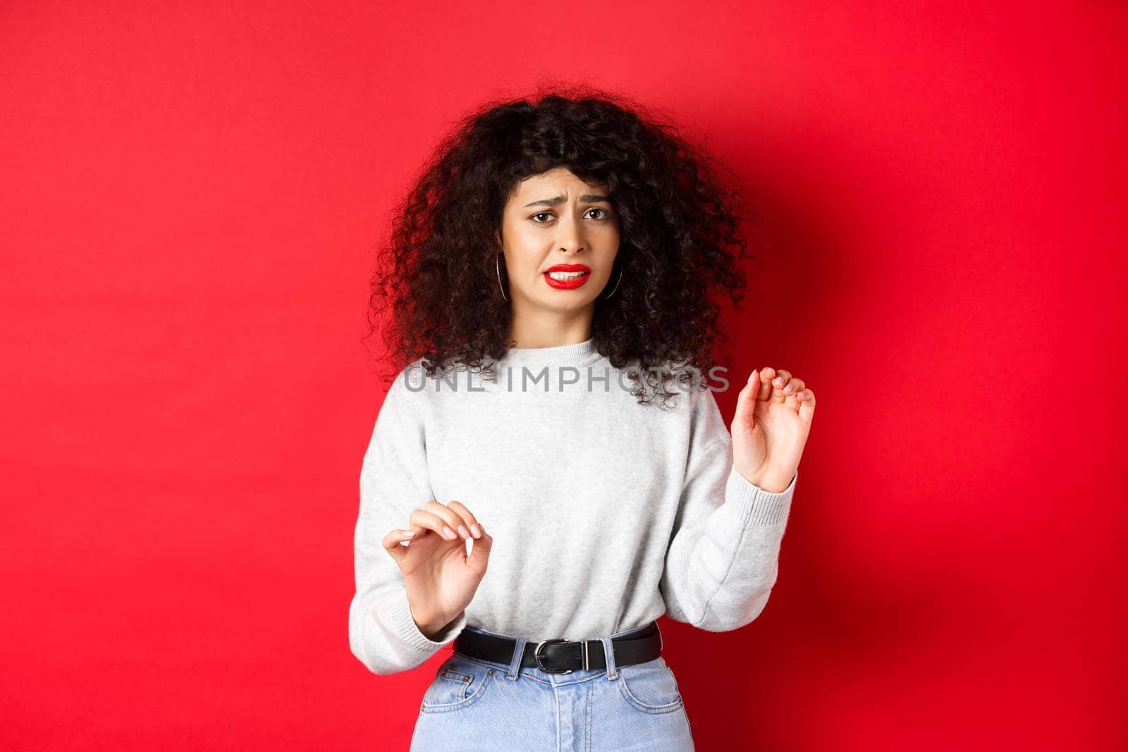 Disgusted and reluctant woman say no, raising hands to block or refuse, asking to stop, looking uncomfortable, standing on red background by Benzoix