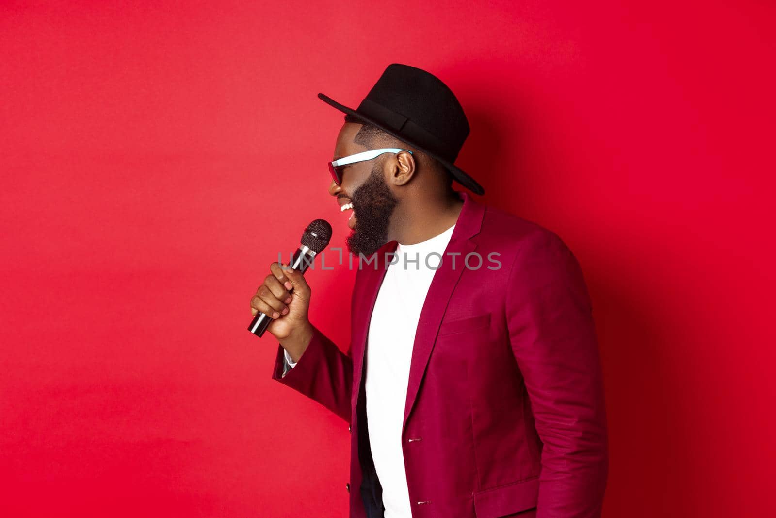 Passionate black male singer performing against red background, singing into microphone, wearing party outfit, standing over red background by Benzoix