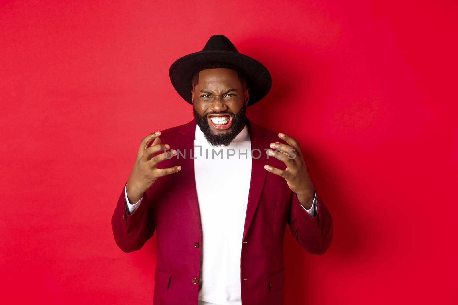 Angry african american man looking aggressive, shaking hands and staring with hatred at camera, red background by Benzoix
