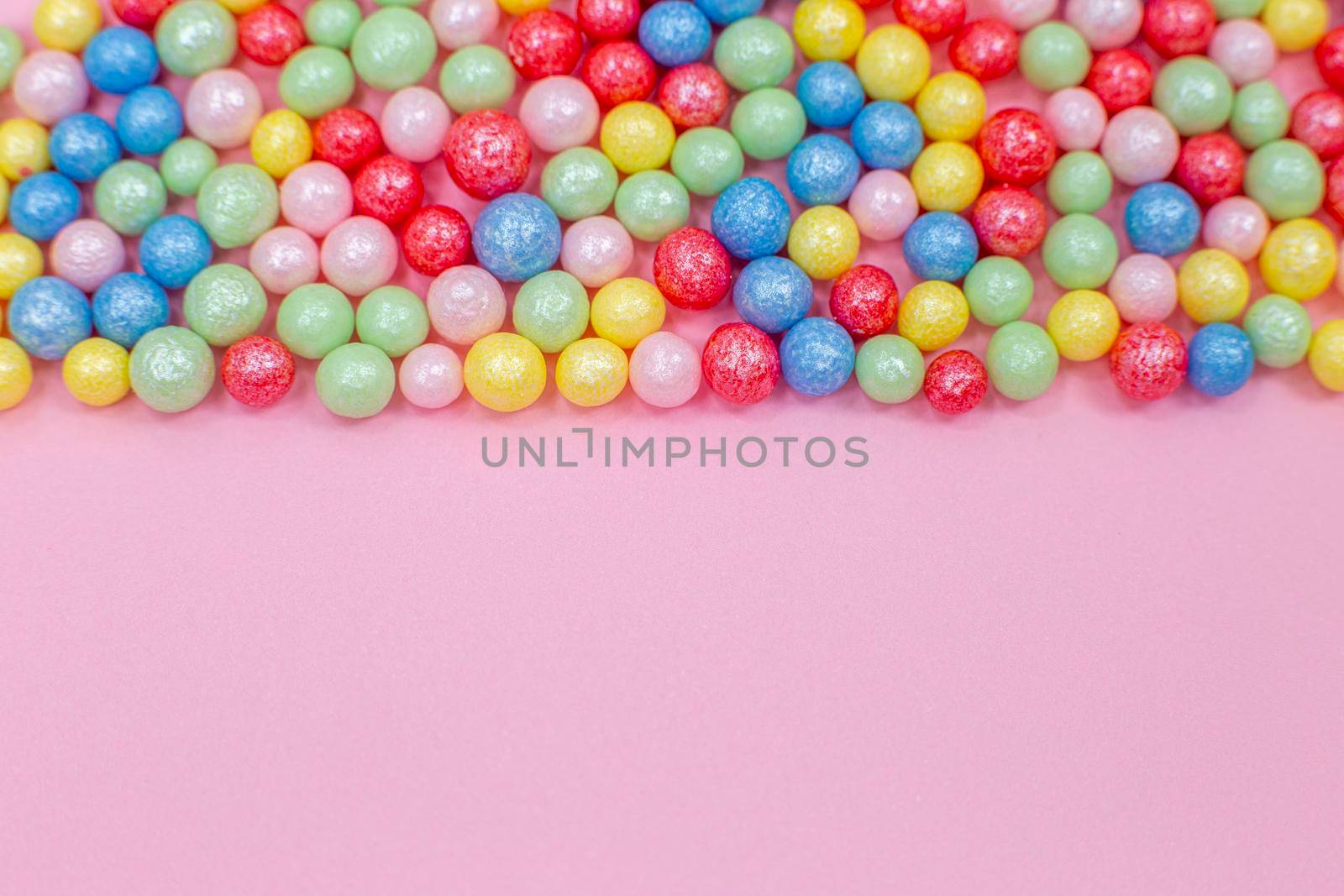 Multi-colored round glossy balls of sugar confectionery topping lie at the top on a pink background.Copy space