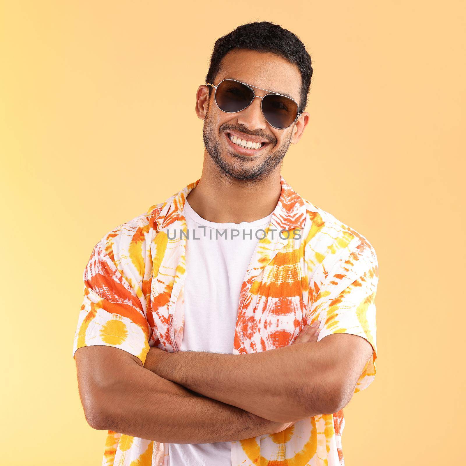 Its vacation time. Shot of a young man wearing glasses and a tie dye shirt while standing against a yellow background. by YuriArcurs