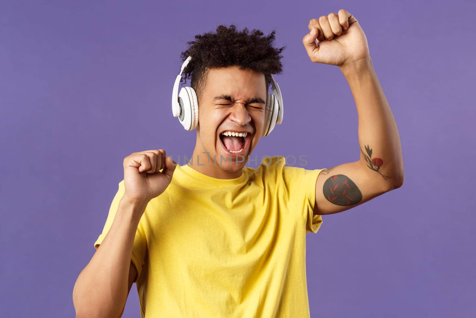 Close-up portrait of cheerful, happy young dancing guy lift hand up singing along, close eyes and smiling upbeat as listening awesome song in headphones, enjoying music, purple background by Benzoix