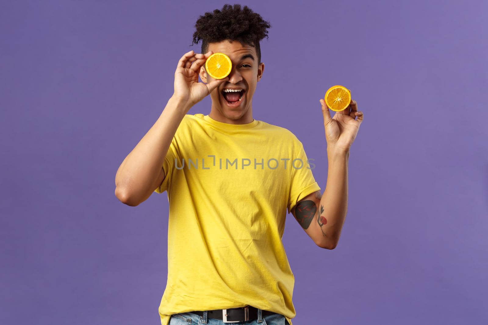 Holidays, vitamins and vacation concept. Portrait of carefree, upbeat good-looking man having fun, look playful laughing, likes eating fruits healthy food, holding pieces of oranges.