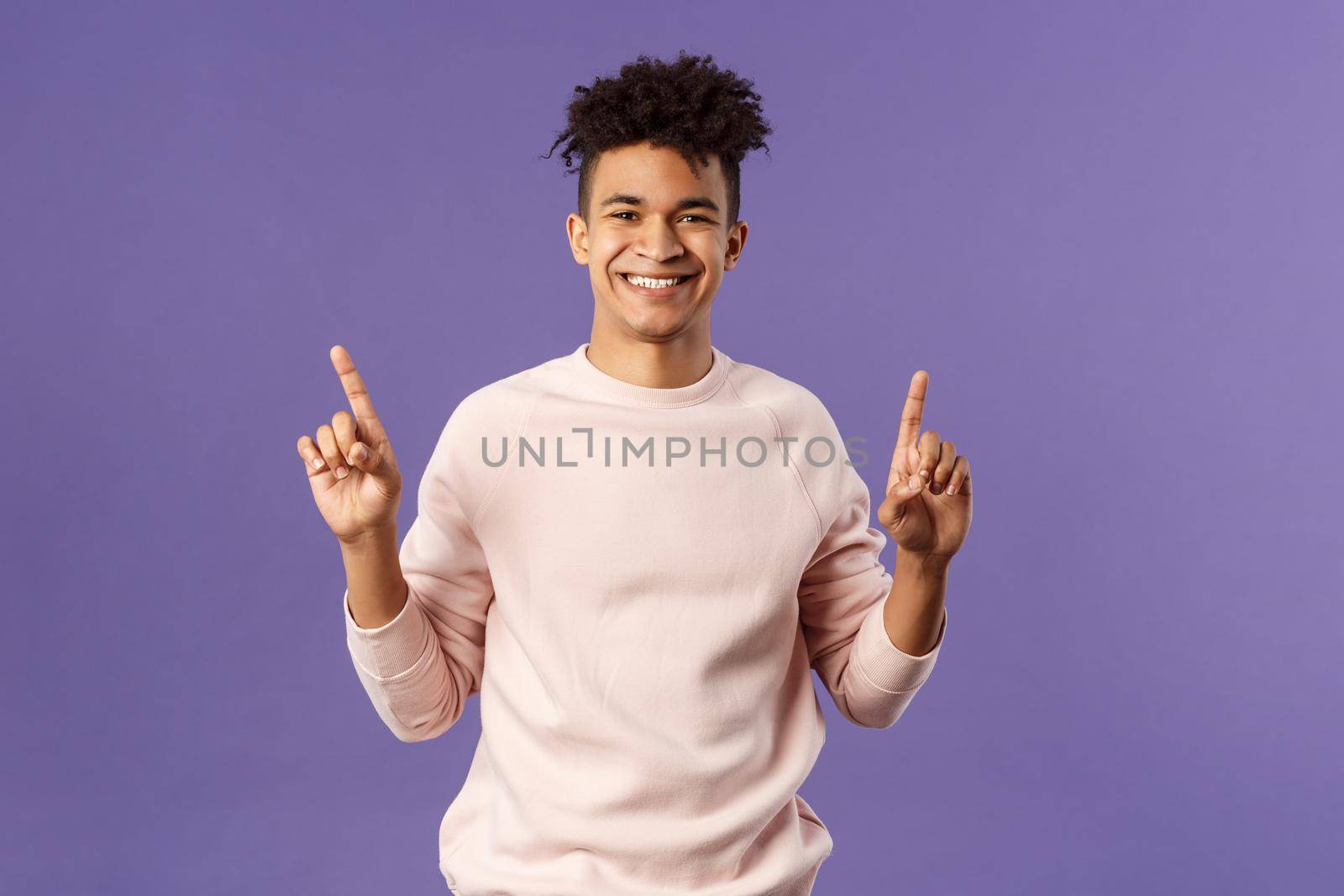 Waist-up portrait of joyful good-looking hispanic man with dreads, promoting product or company banner hanging on top, pointing fingers up, smiling satisfied, recommend subscribe or click link.