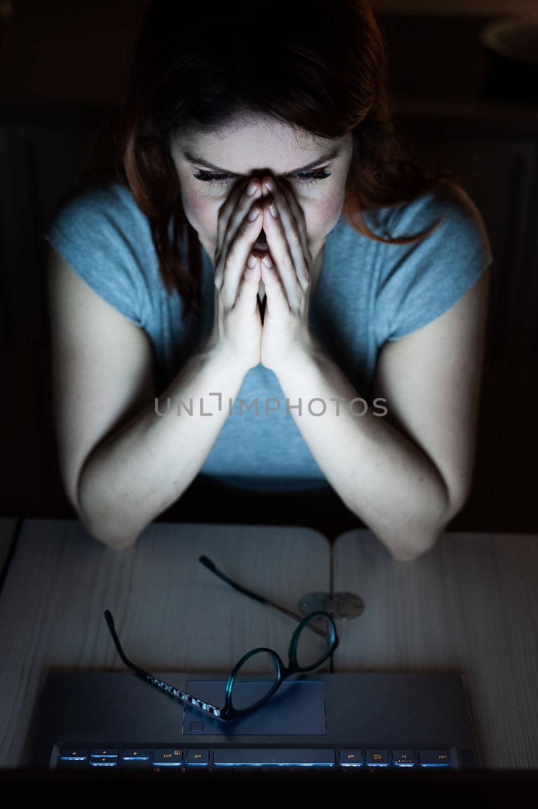 Tired, exhausted woman in frustration working overtime on a laptop. A female freelancer in desperation holds his hands by his face. Night work from home. Deadline by mrwed54