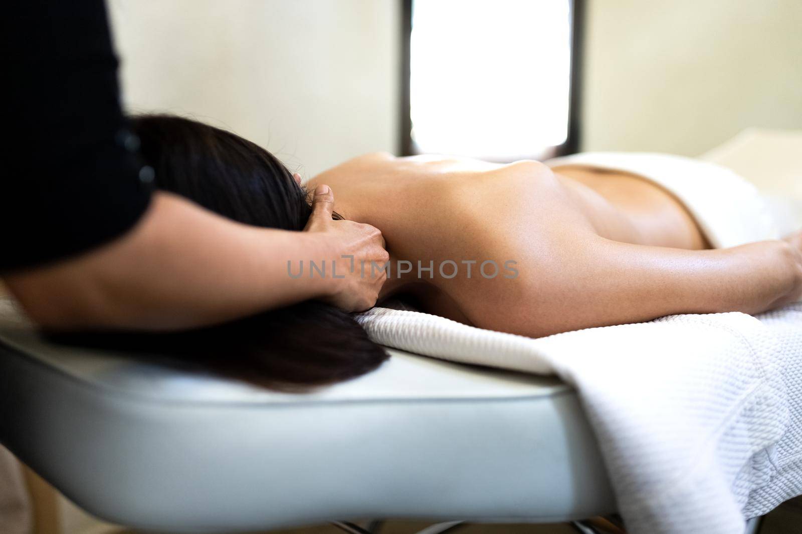 Unrecognizable massage therapist giving neck massage to female client. Bodycare concept.