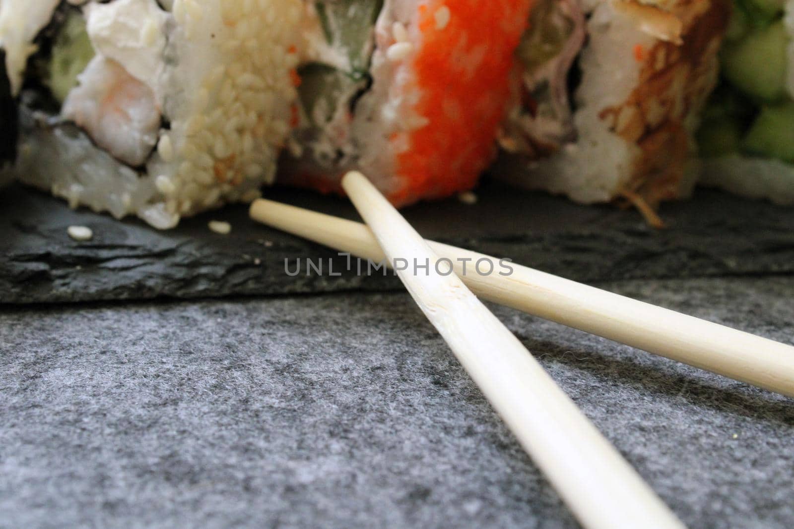Rolls with shrimp, sesame, tuna, bacon, cheese, cucumber, vegetables and sushi sticks on a black board. Close-up. Japanese cuisine. Background.
