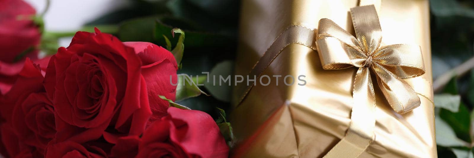 Gift in gold package with bow lying on bouquet of red roses closeup by kuprevich