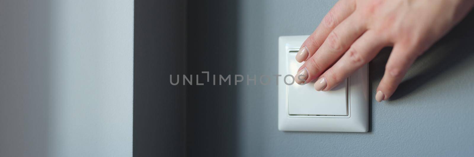 Female hand pressing light switch in apartment closeup. Energy savings concept