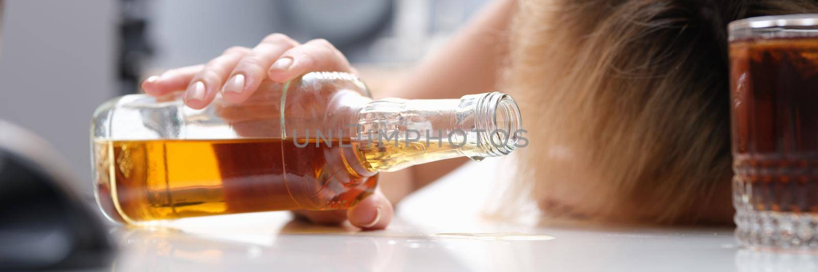 Woman sleeping at table with bottle of alcohol in her hands closeup. Alcohol addiction in women concept