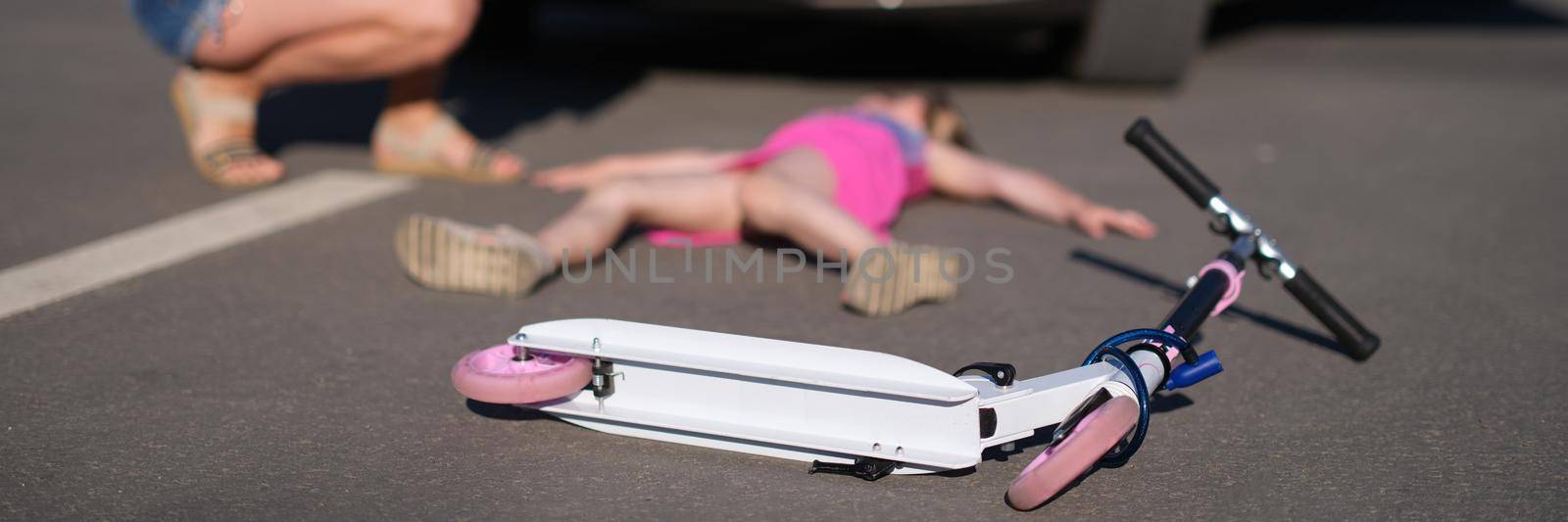 Little girl lies motionless on asphalt with scooter after collision with car.