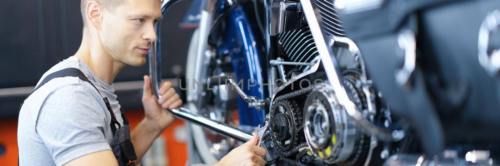 Male car mechanic holds wrench and looks at open motorcycle engine. High-quality motorcycle repair and maintenance concept