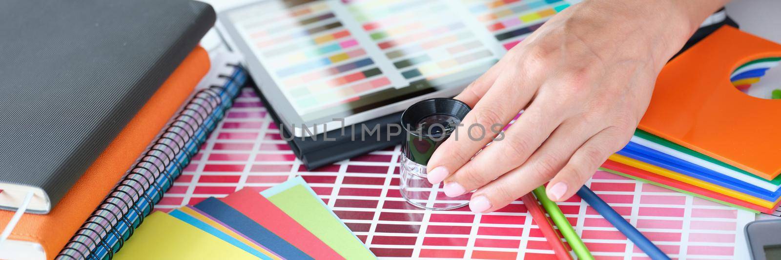Woman designer looks through magnifying glass at color palette with different shades of colors. Color matching concept