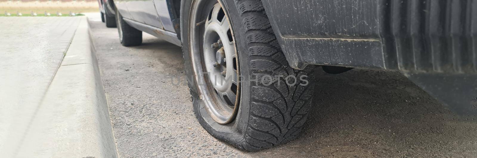 Car with flat tire standing near sidewalk closeup. Tire repair and maintenance concept