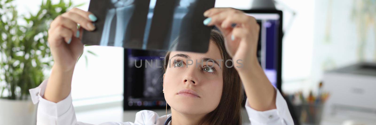 Woman doctor looking at xray of hand in clinic office by kuprevich