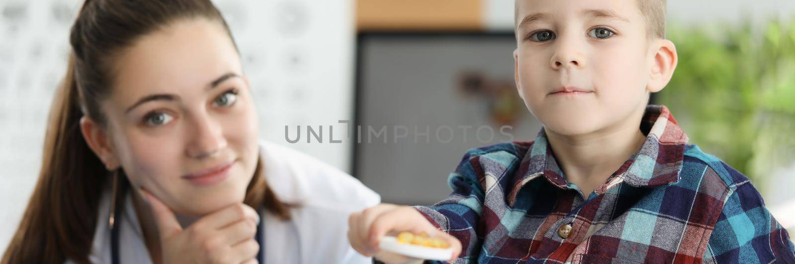 Little boy holding yellow gelatin capsules at doctor appointment. Taking vitamin D and preventing rickets in children concept