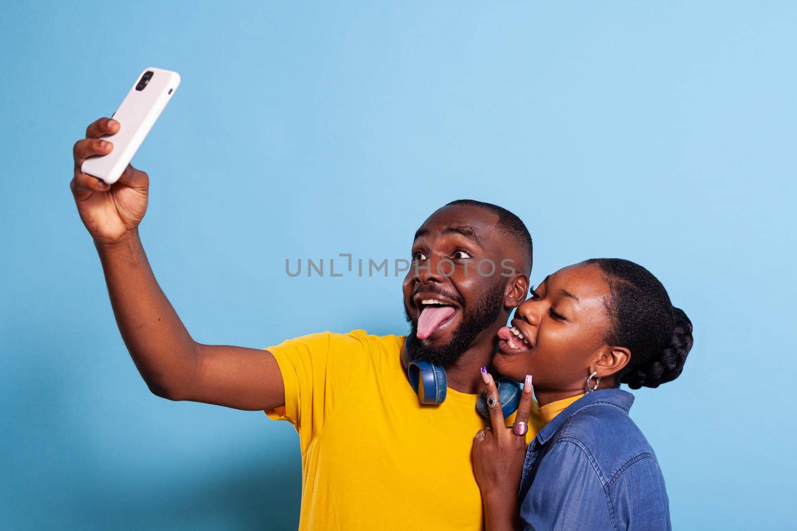 Goofy couple sticking tongue out and taking pictures on smartphone by DCStudio