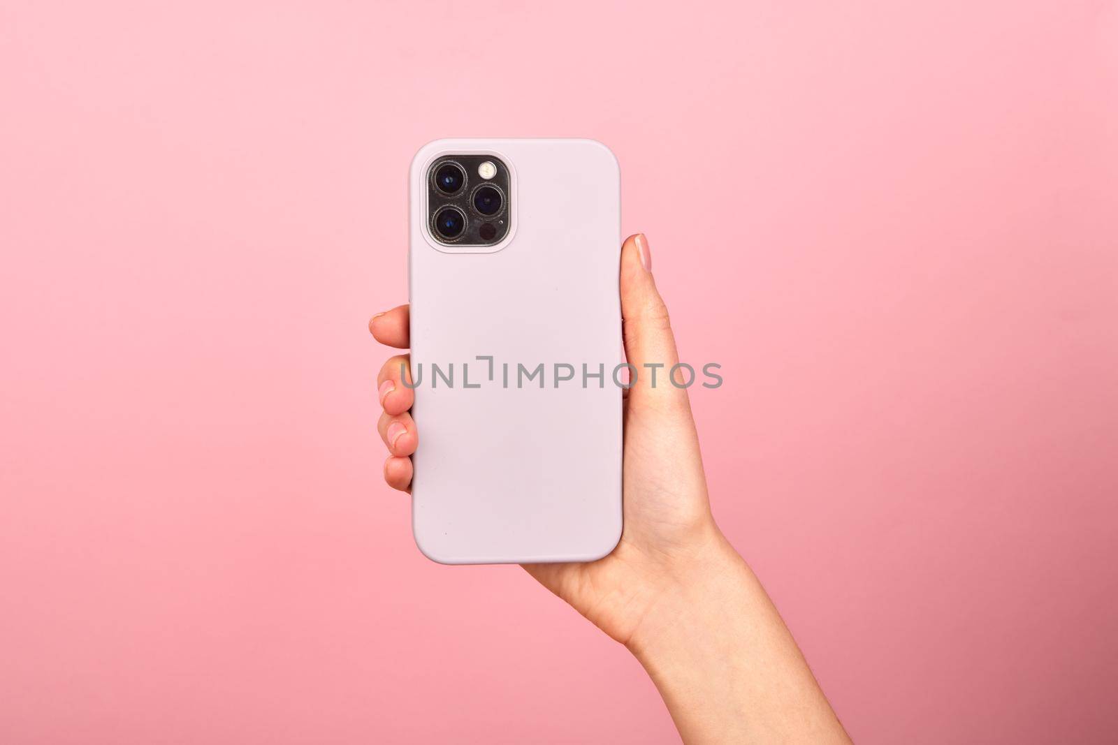 Female hand holding white smartphone in soft silicone cover back view . Phone case mock up isolated on pink background