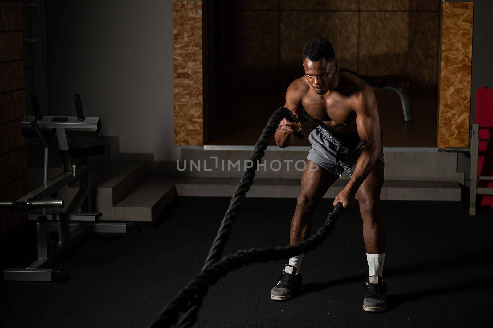 Attractive african american man with naked torso doing endurance exercises with trope. by mrwed54