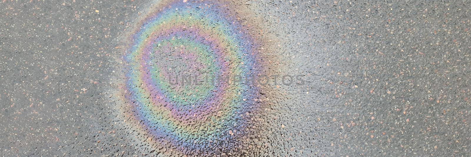 Rainbow stain on wet asphalt from machine oil closeup background. Environmental protection concept