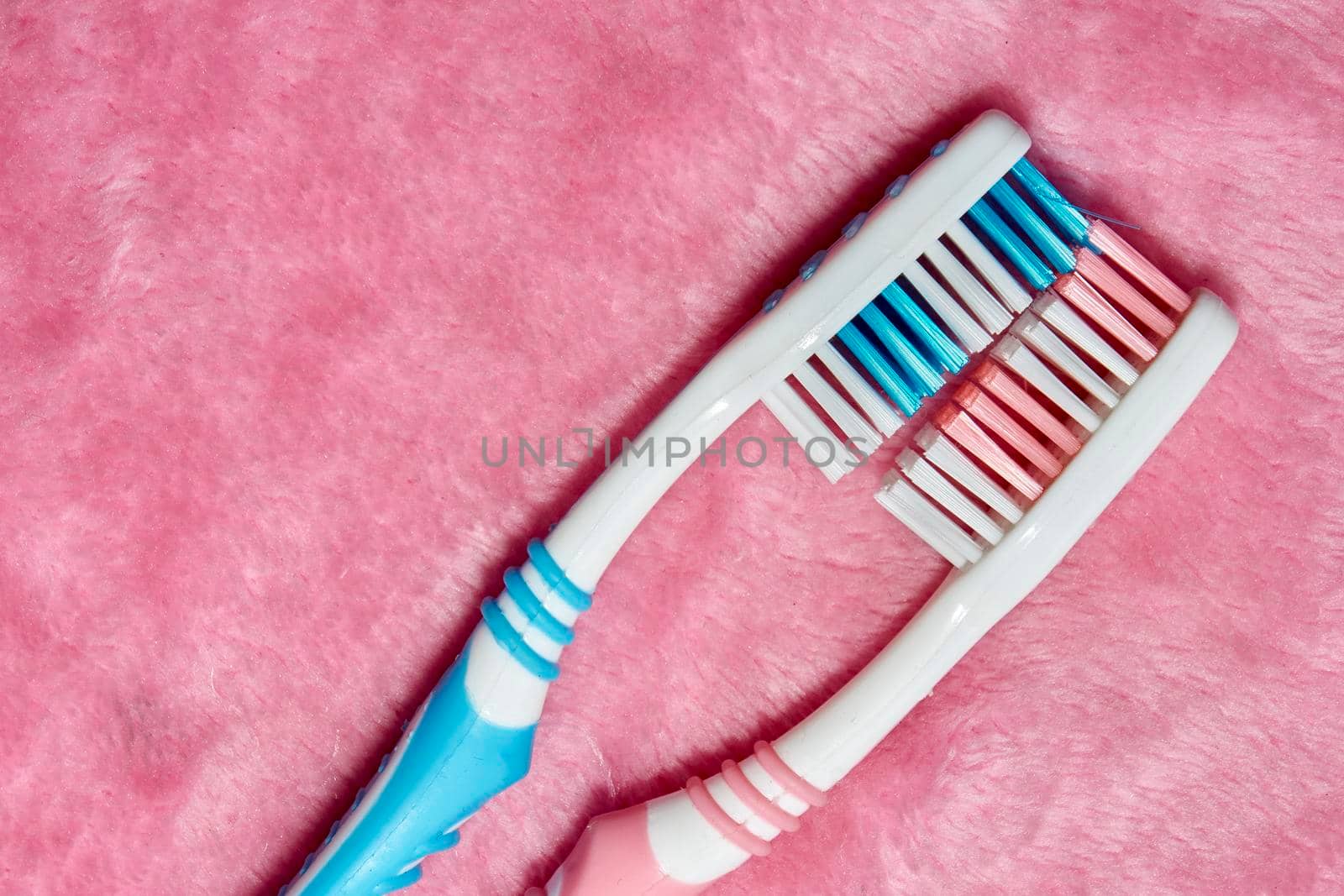 a small brush with a long handle, used for cleaning the teeth.Two toothbrushes on a pink fluffy towel