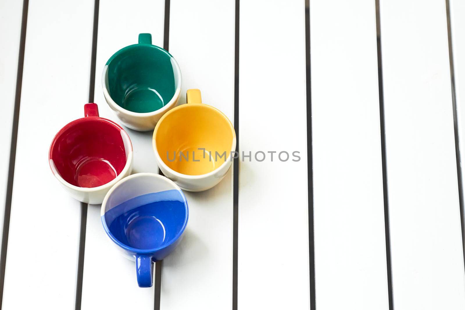 a small bowl-shaped container for drinking from, typically having a handle.Four cups on a white striped table.