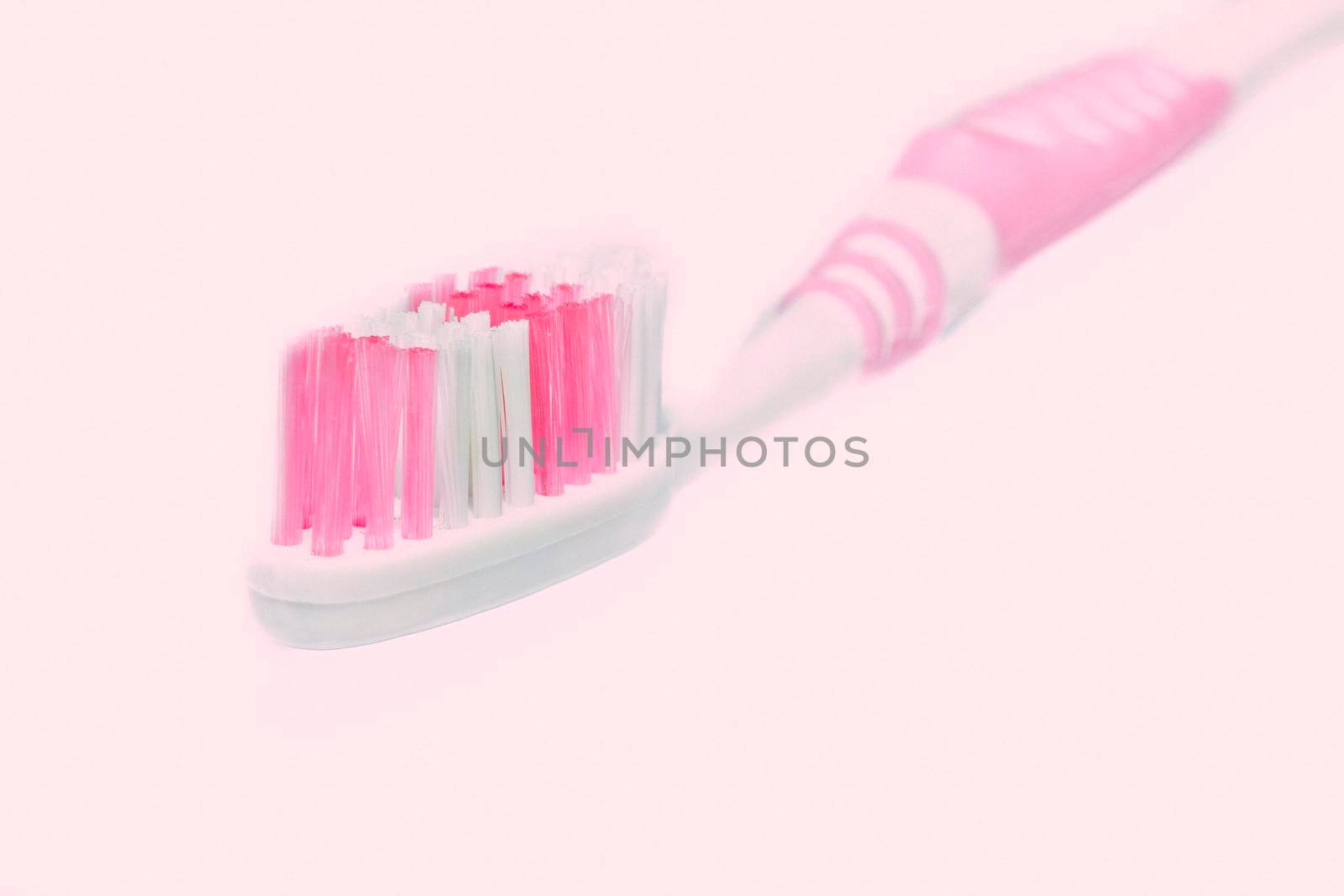 a small brush with a long handle, used for cleaning the teeth. Pink toothbrush on pale pink background close up.