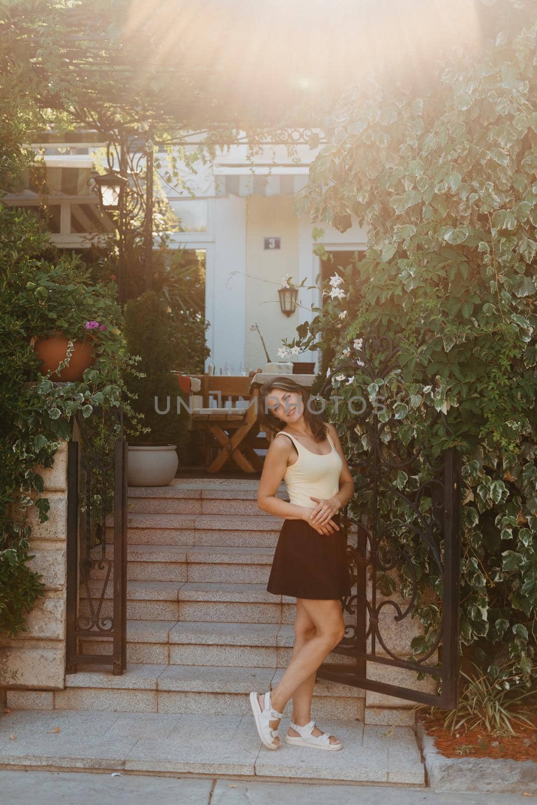 Girl tourist walking through ancient narrow street on a beautiful summer day in MEDITERRANEAN MEDIEVAL CITY , OLD TOWN bUDVA, MONTENEGRO. Young beautiful cheerful woman walking on old street at tropical town. Pretty girl looking at you and smiling